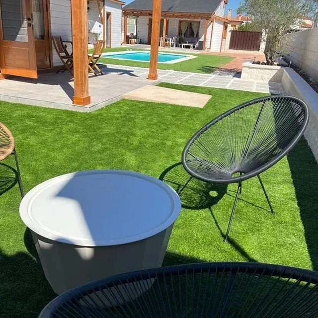 Un césped con sillas y una mesa frente a una casa.