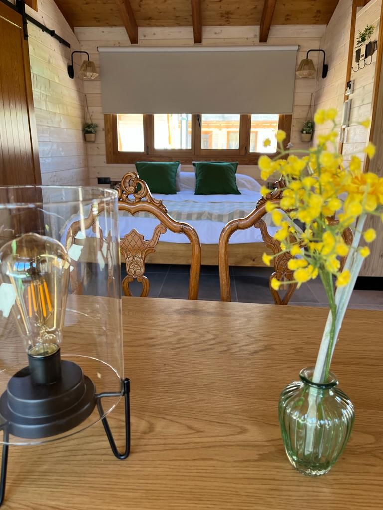 Un jarrón de flores amarillas está sobre una mesa de madera frente a una cama.