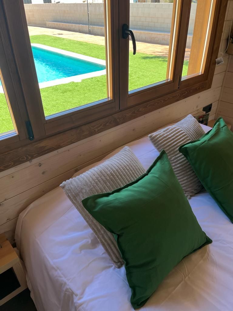 Una cama con almohadas verdes y una ventana con vistas a una piscina.
