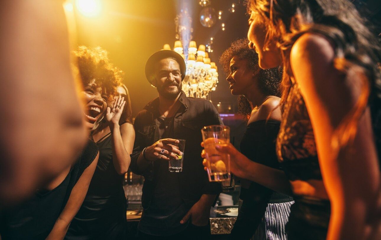 Un grupo de personas están de pie en un club sosteniendo bebidas.
