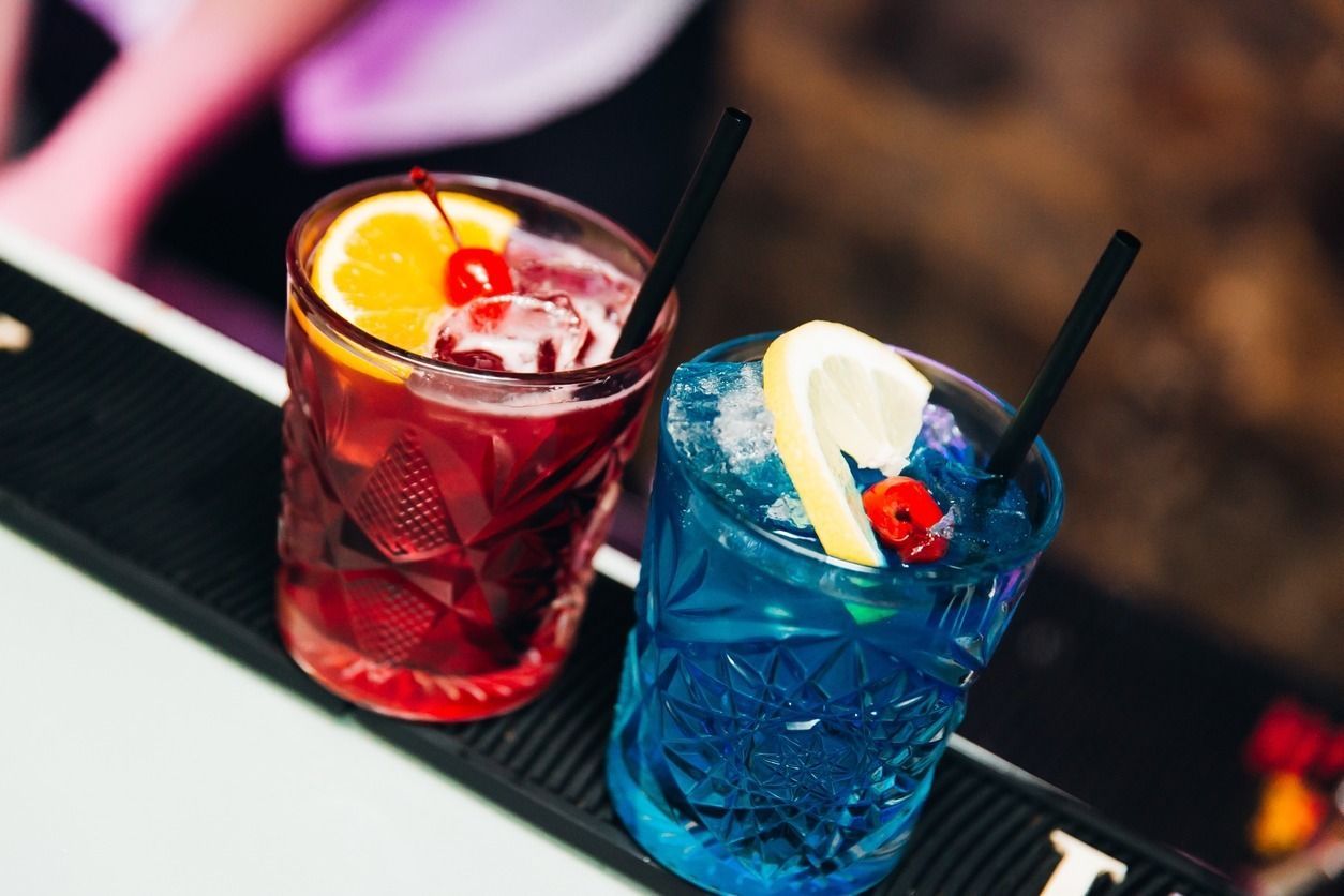 Hay dos bebidas de diferentes colores en una barra.