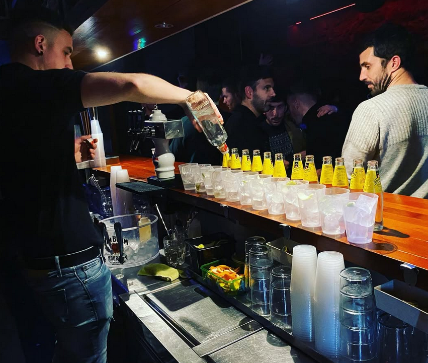 Un camarero sirve una bebida en una fila de vasos de chupito.