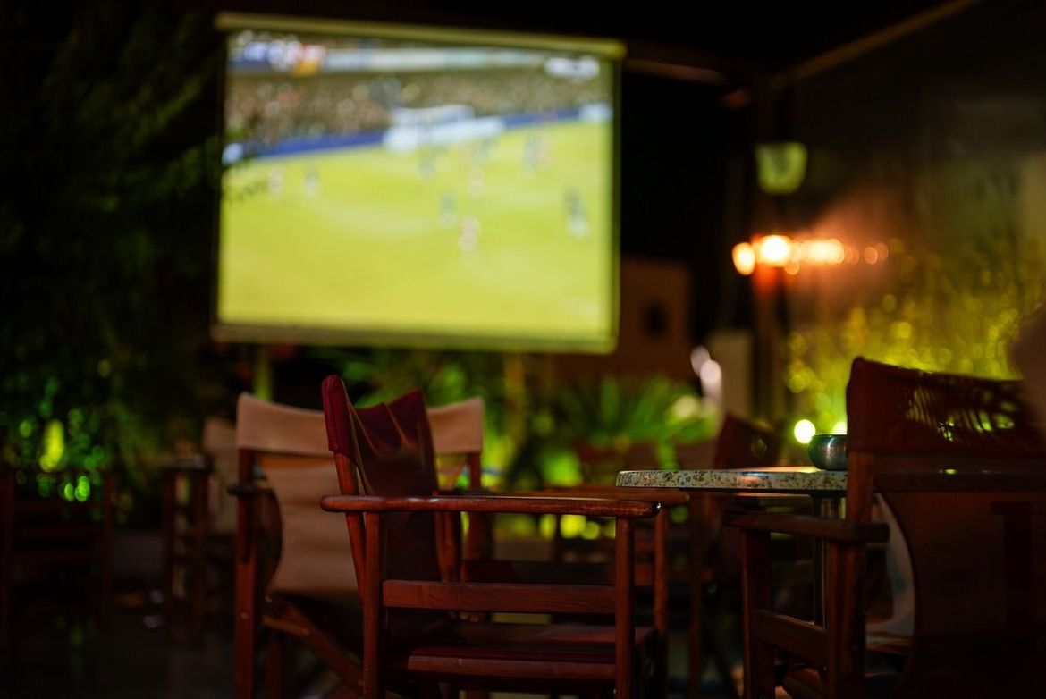 Una pantalla de proyector proyecta un partido de fútbol en un patio por la noche.