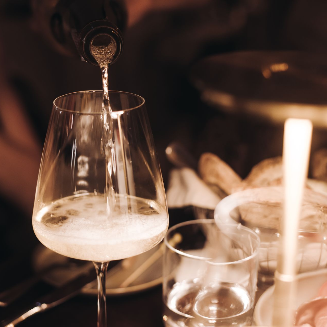 Du vin est versé dans un grand verre, une table est dressée avec du pain.