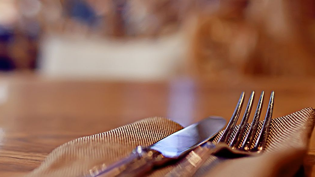 Fourchette et couteau sur une serviette brune pliée, dressés sur la table.