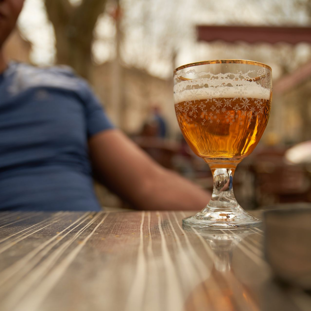 Un verre de bière sur une table, avec une personne en extérieur.