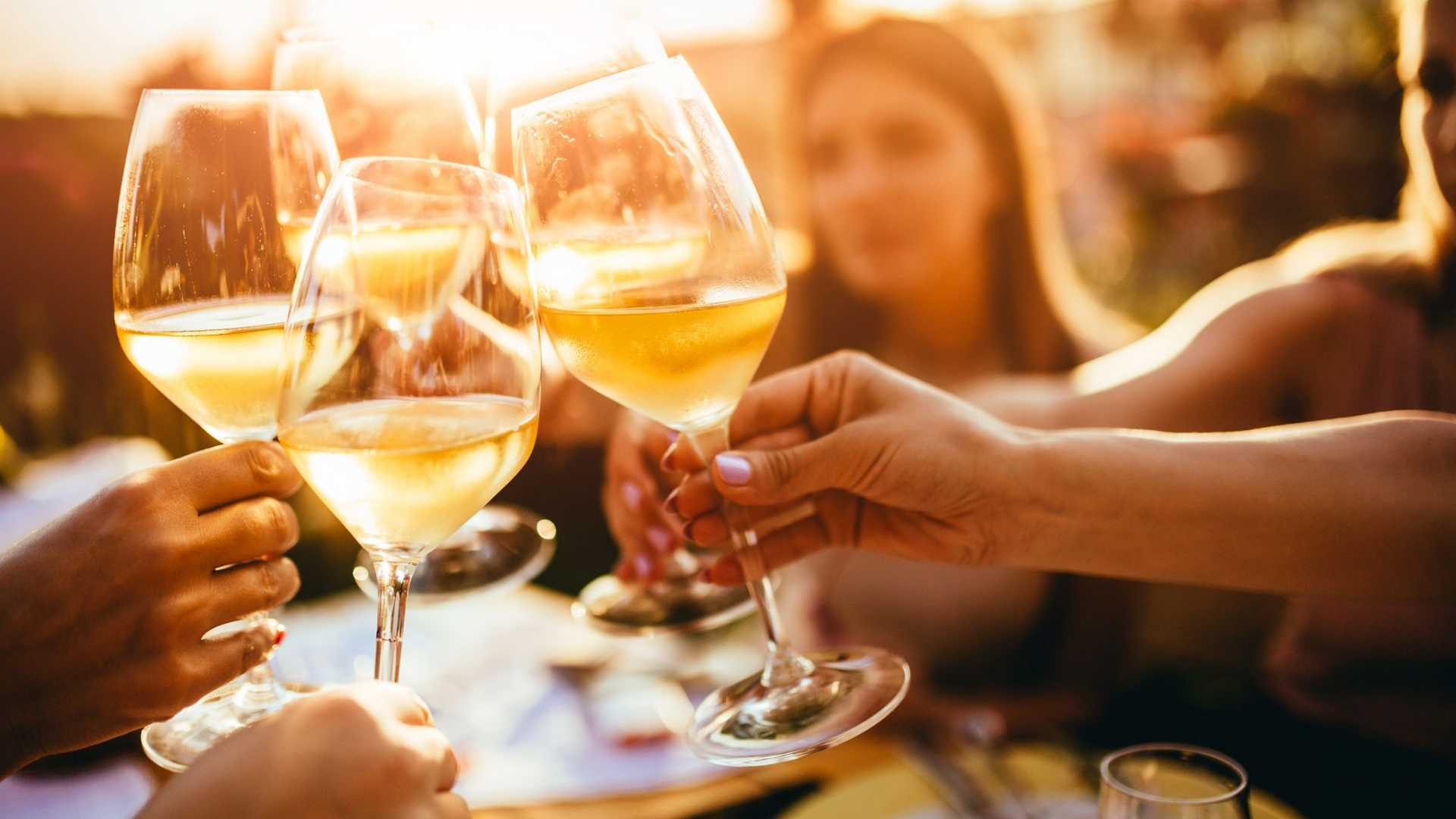 Des gens trinquent avec des verres de vin blanc en terrasse.