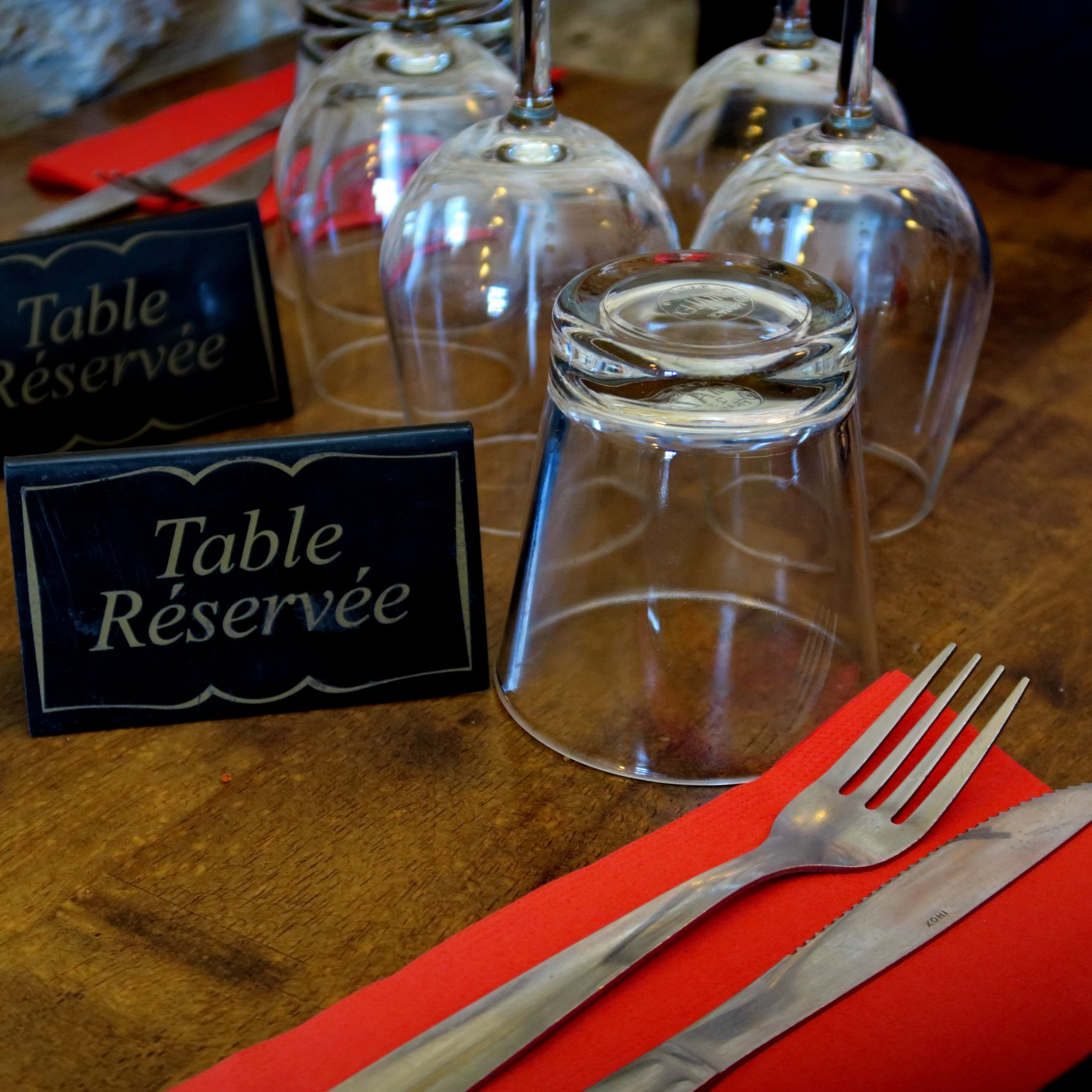 Dressage de table avec des verres à l'envers, des couverts sur une serviette rouge et des panneaux Table réservée.