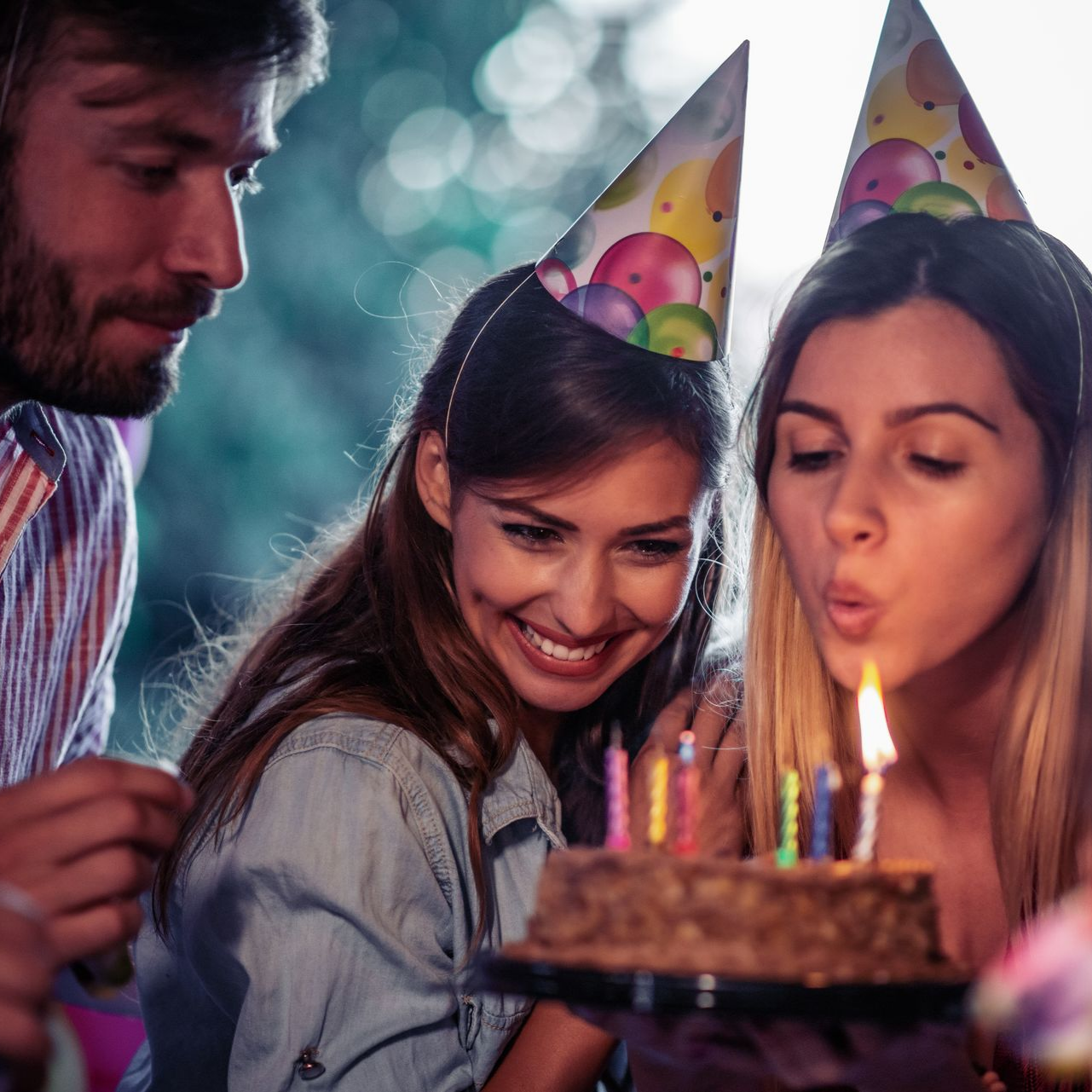 Une femme souffle les bougies de son gâteau d'anniversaire, souriant avec ses amis lors d'une fête.