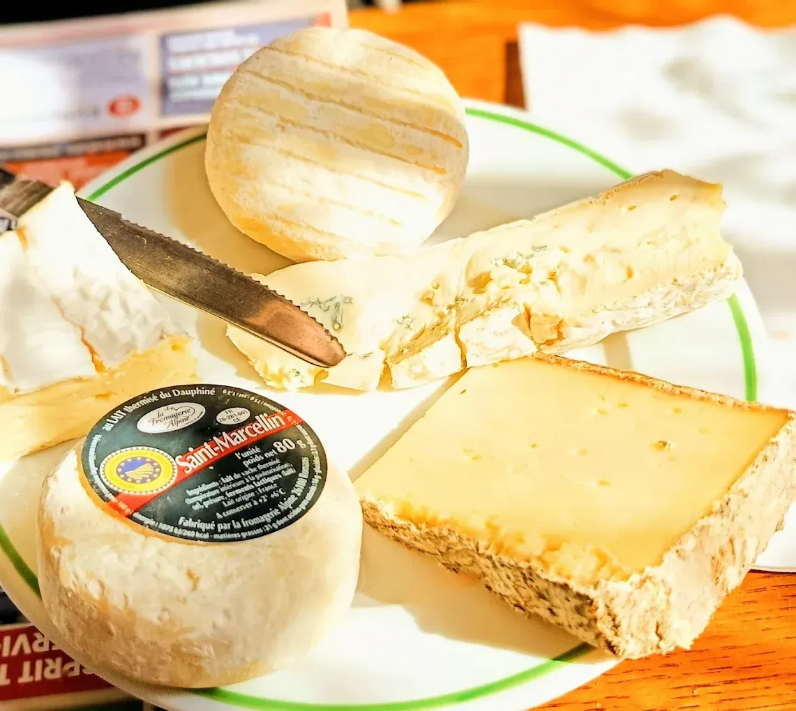 Assiette de trois fromages : brie, fromage à pâte dure et fromage bleu sur une table.