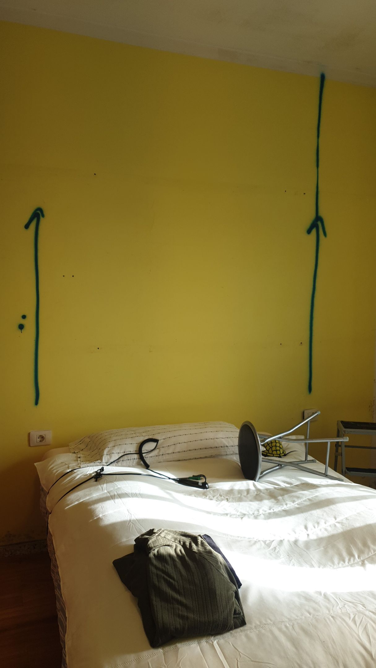 Una cama está frente a una pared amarilla con flechas pintadas en ella.