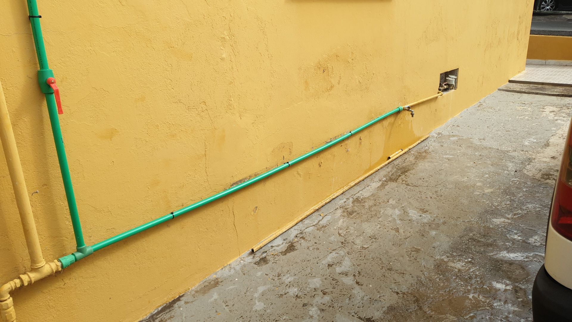Una pared amarilla con tuberías verdes adheridas a ella.
