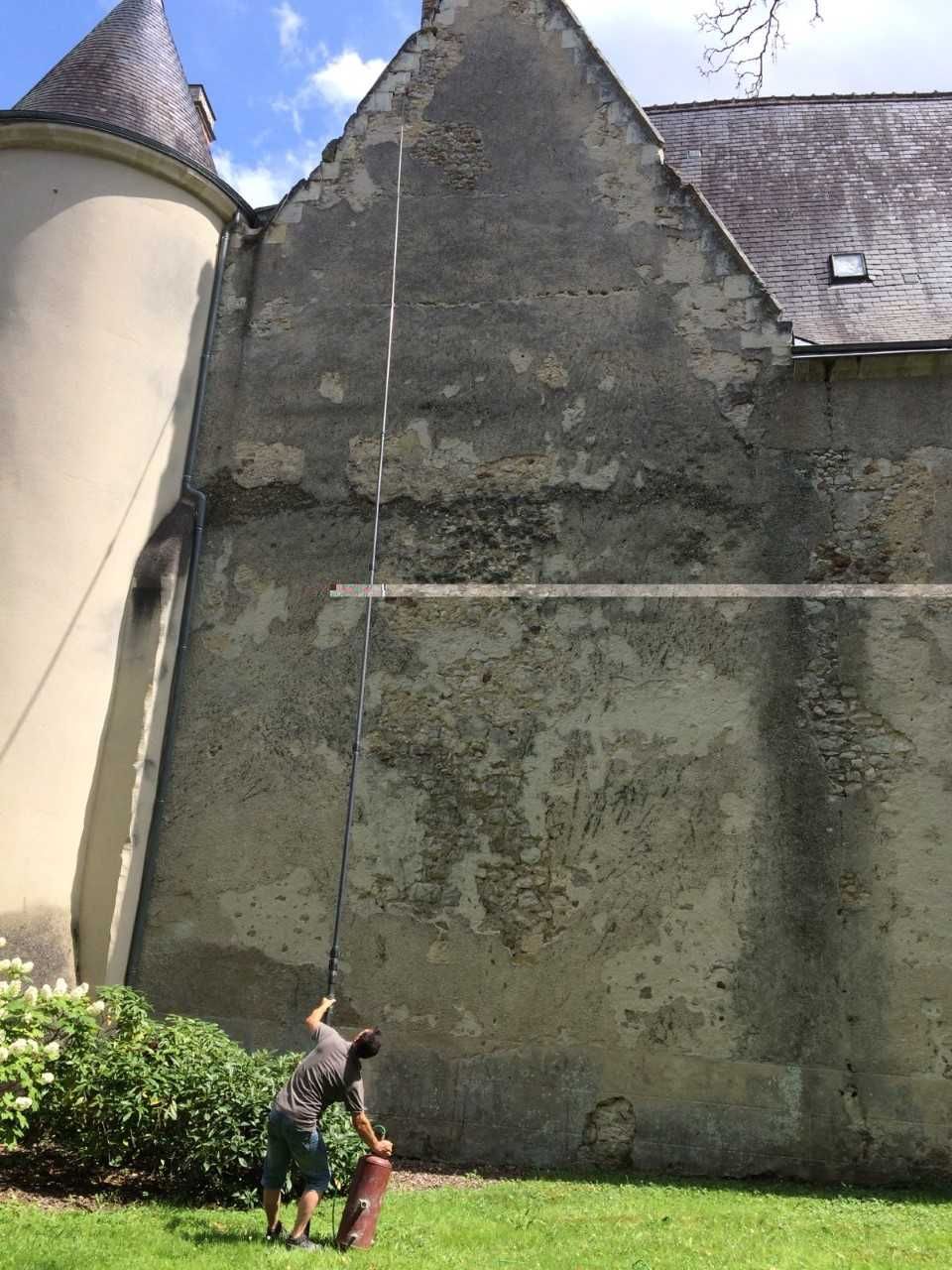 Une personne se tient à côté d'un grand bâtiment en pierre et utilise une perche téléscopique pour lutter contre des nuisibles
