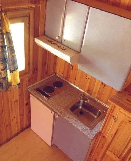 Cocina compacta con paneles de madera, estufa, fregadero, armarios y puerta con ventana.