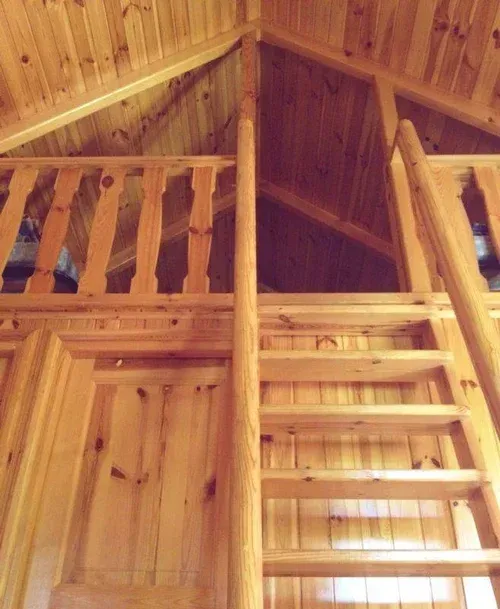 Interior de un altillo de madera con una escalera que conduce a una zona de descanso superior.