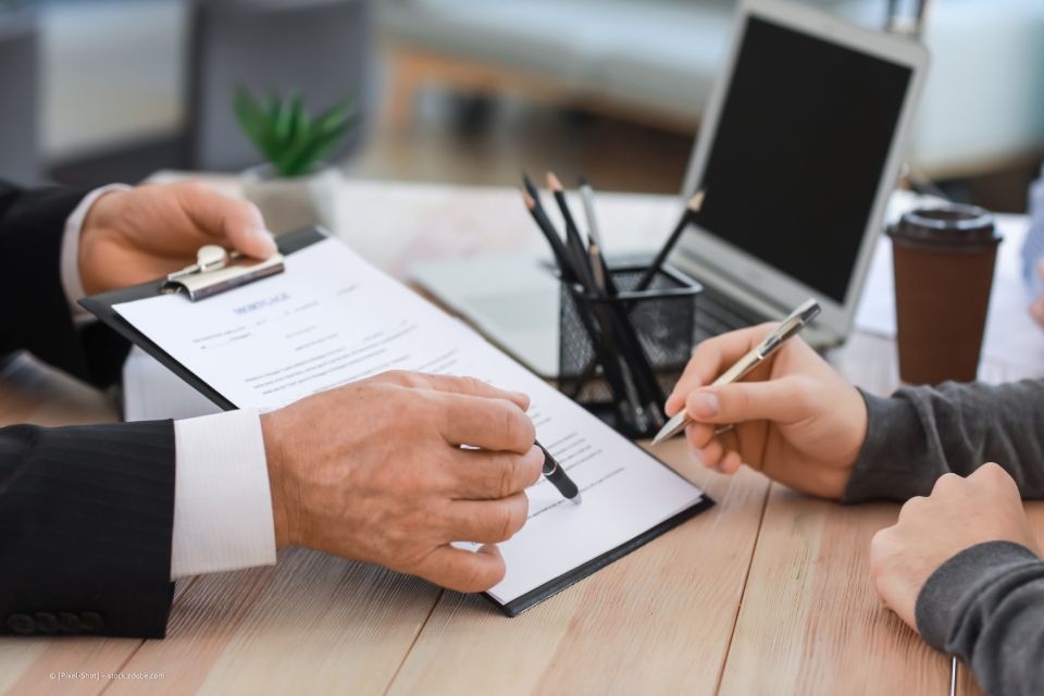ATM Rechts- und Steuerberatungsgesellschaft – eine Person deutet mit einem Kugelschreiber auf eine Stelle auf einem Dokument hin, eine zweite Person setzt dort eine Unterschrift.