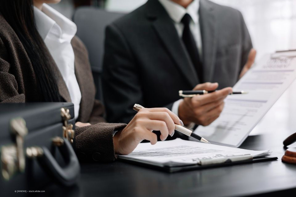 ATM Rechts- und Steuerberatungsgesellschaft – ein Mann im Anzug und eine Frau sitzen mit Schnellheftern und Kugelschreiber in der Hand an einem Tisch.