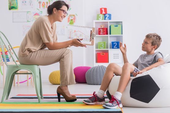 Una mujer está sentada en una silla hablando con un niño pequeño que está sentado en un sillón puf.