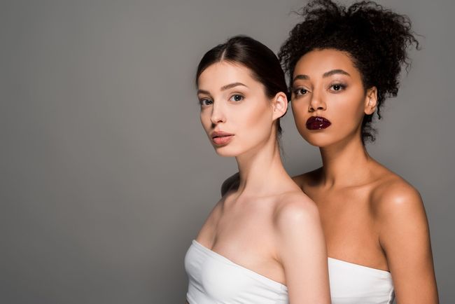 Dos hermosas mujeres están paradas una al lado de la otra sobre un fondo gris.