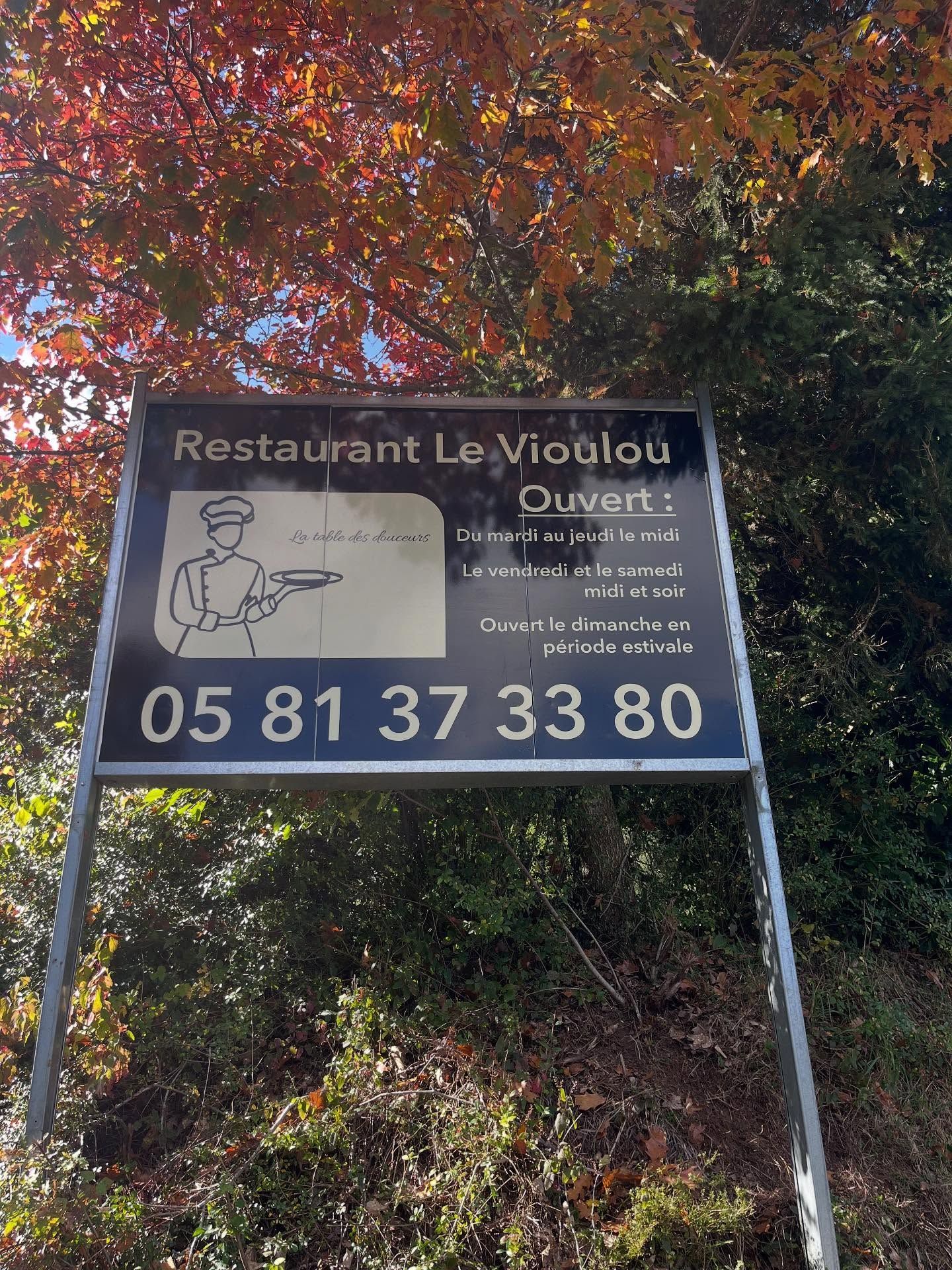Une enseigne noire pour Restaurant Le Vioulou avec un dessin de chef.