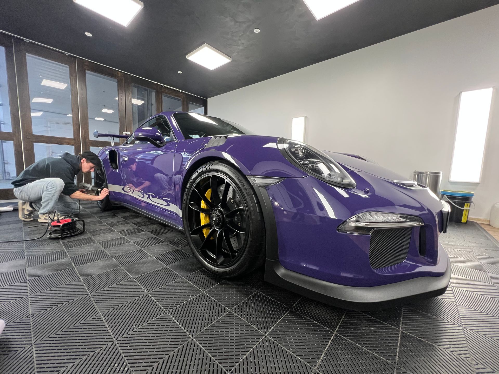 Une personne installe un kit adhésif sur une Porsche violette  dans un studio de detailing automobile professionnel et lumineux.