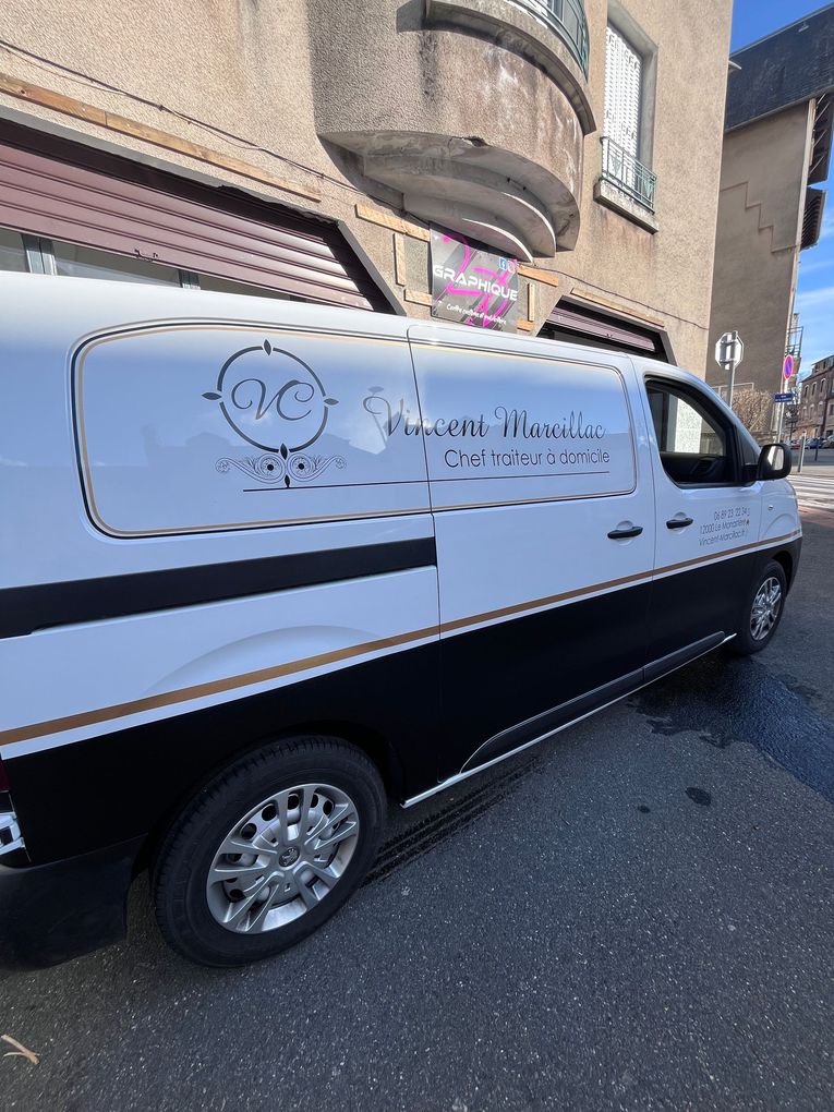 Une camionnette blanche et noire, portant le logo et le texte d'une entreprise sur le côté, est garée sur une rue asphaltée devant un bâtiment.