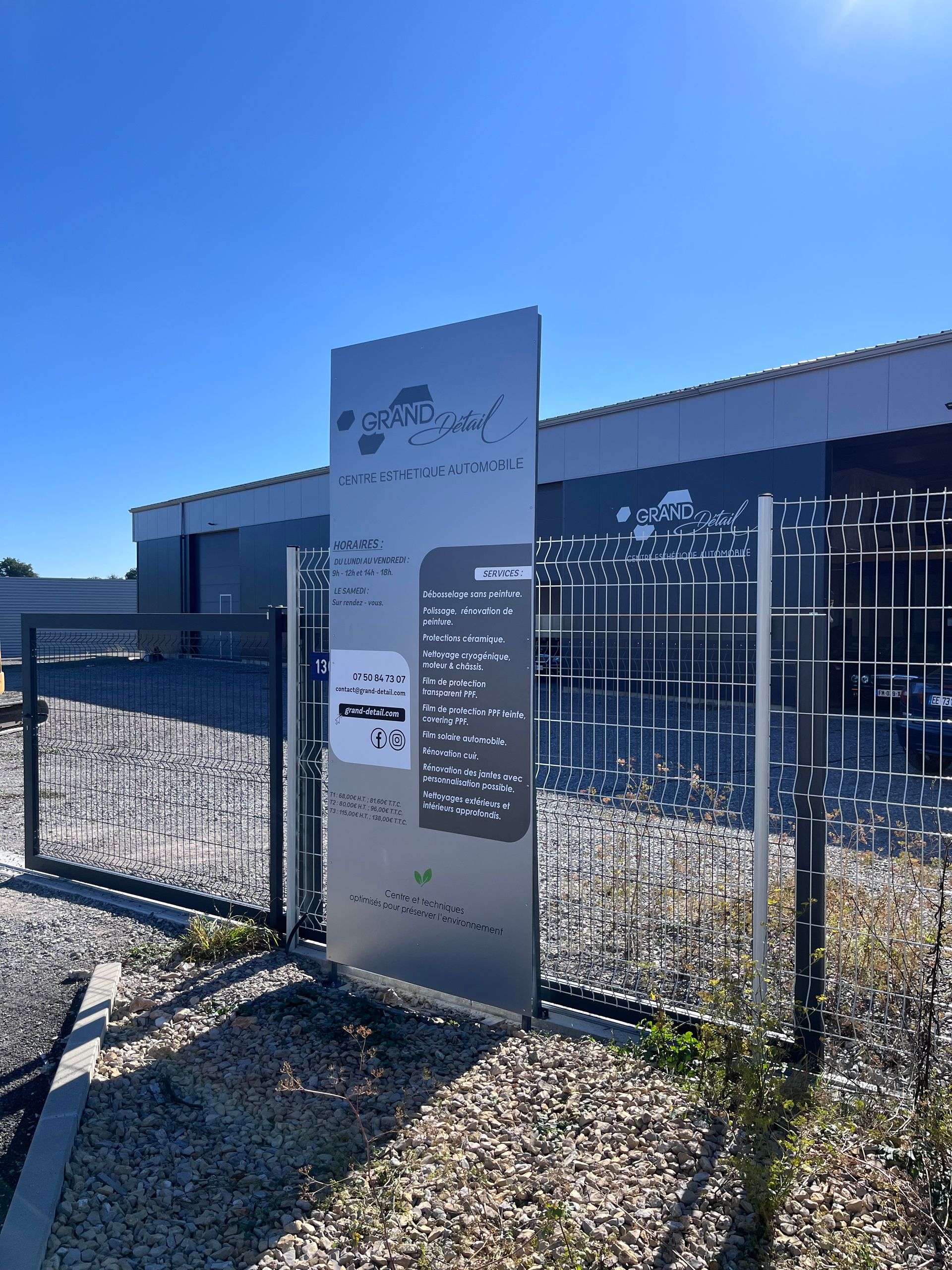 Par une journée ensoleillée, un panneau vertical gris portant du texte se dresse devant un entrepôt industriel moderne.