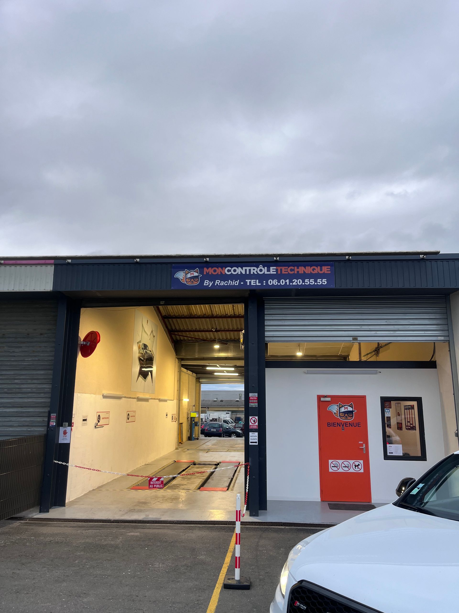 L'entrée d'un garage automobile sous un ciel nuageux, avec un espace ouvert et une porte orange vif.