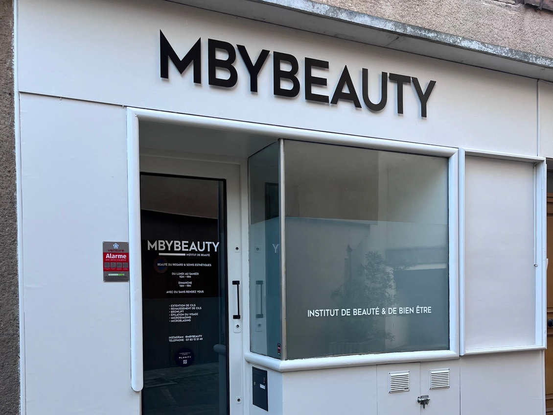 La façade du magasin MBYBEAUTY, un bâtiment blanc avec des lettres noires et une porte vitrée, situé dans une rue.