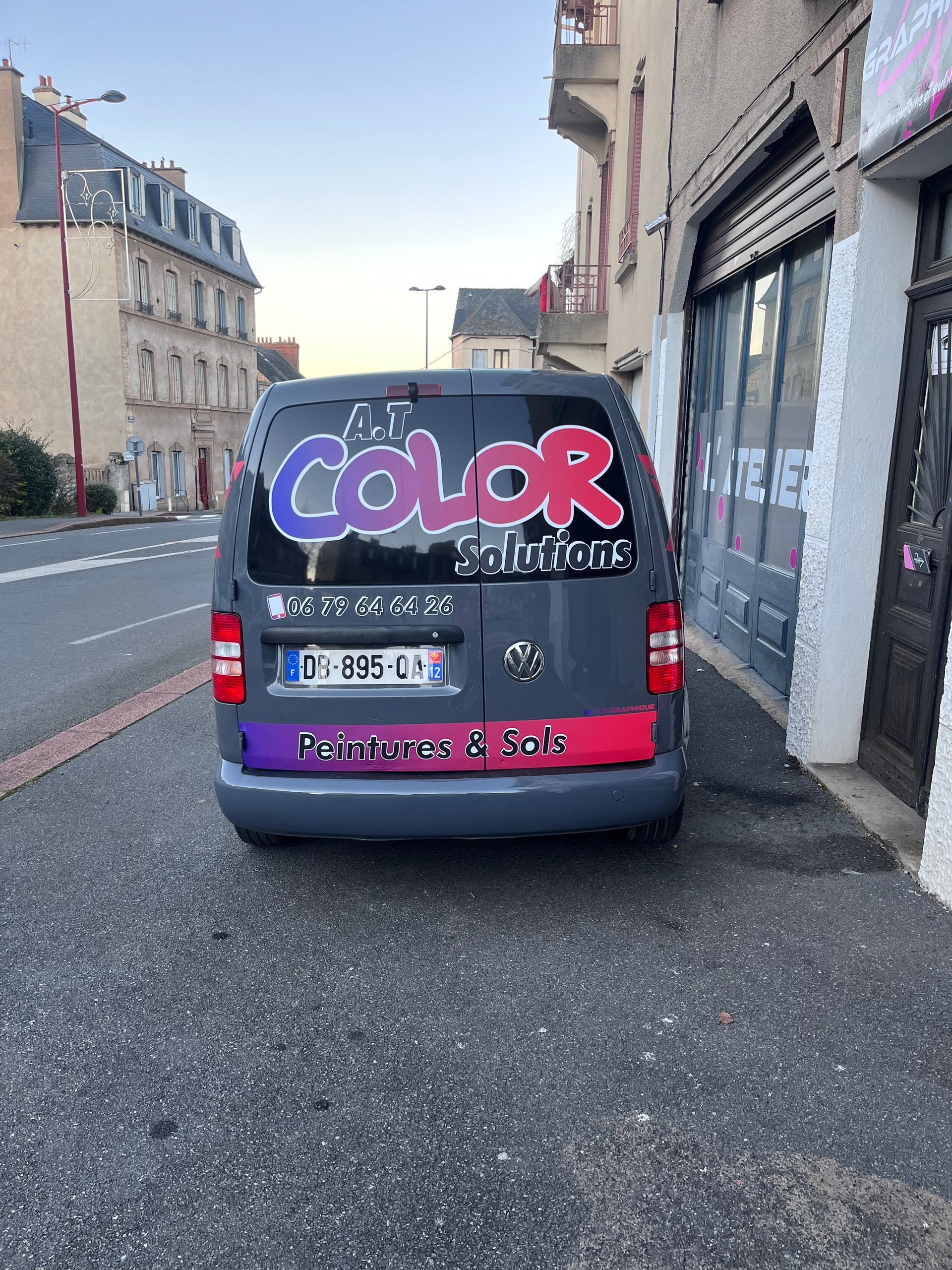 Une camionnette grise garée dans la rue, arborant un grand logo Color Solutions et des inscriptions colorées sur la lunette arrière et le pare-chocs.