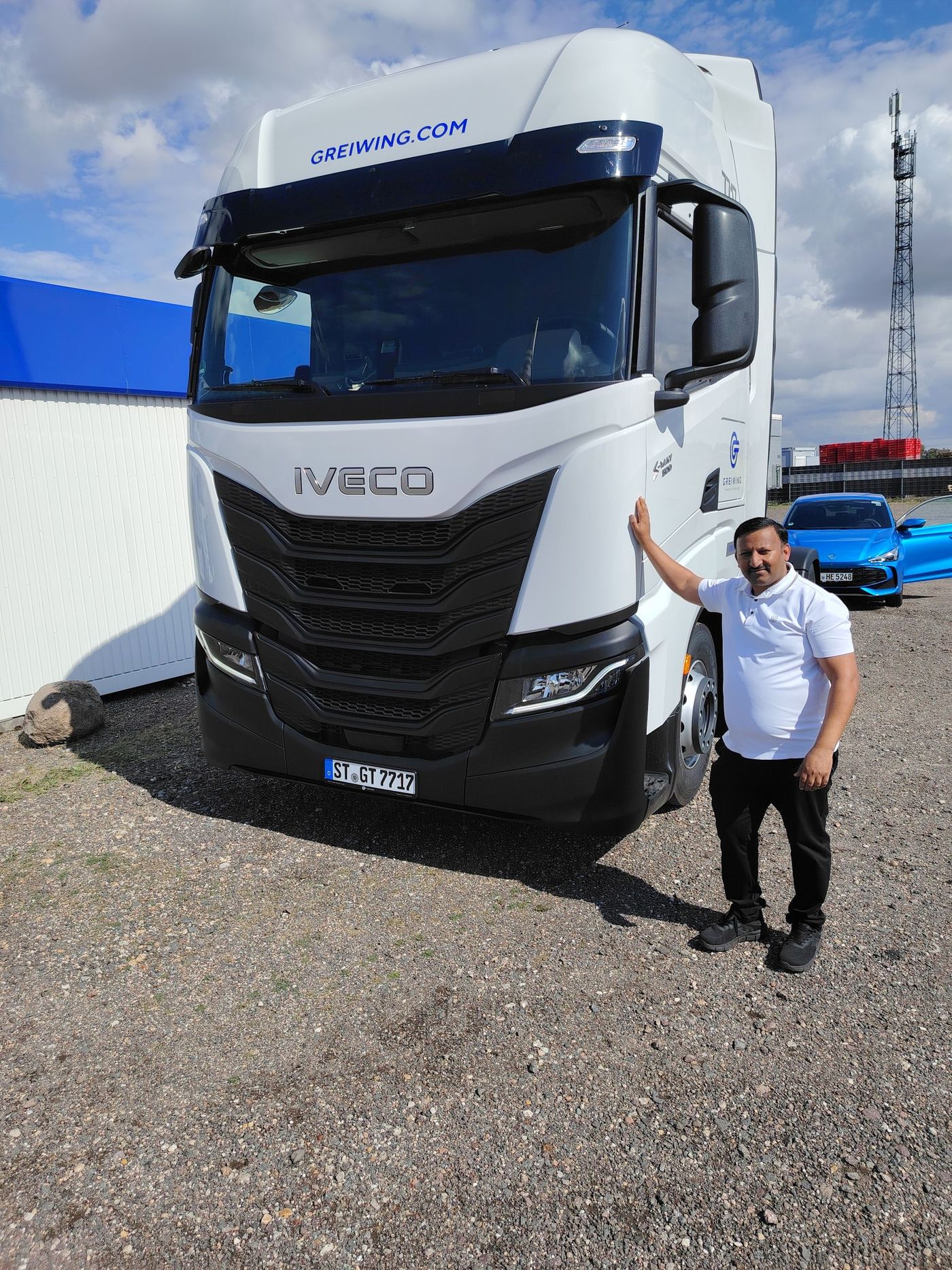 Mann steht neben einem weißen IVECO-Truck mit schwarzem Kühlergrill; sonnige Umgebung im Freien.