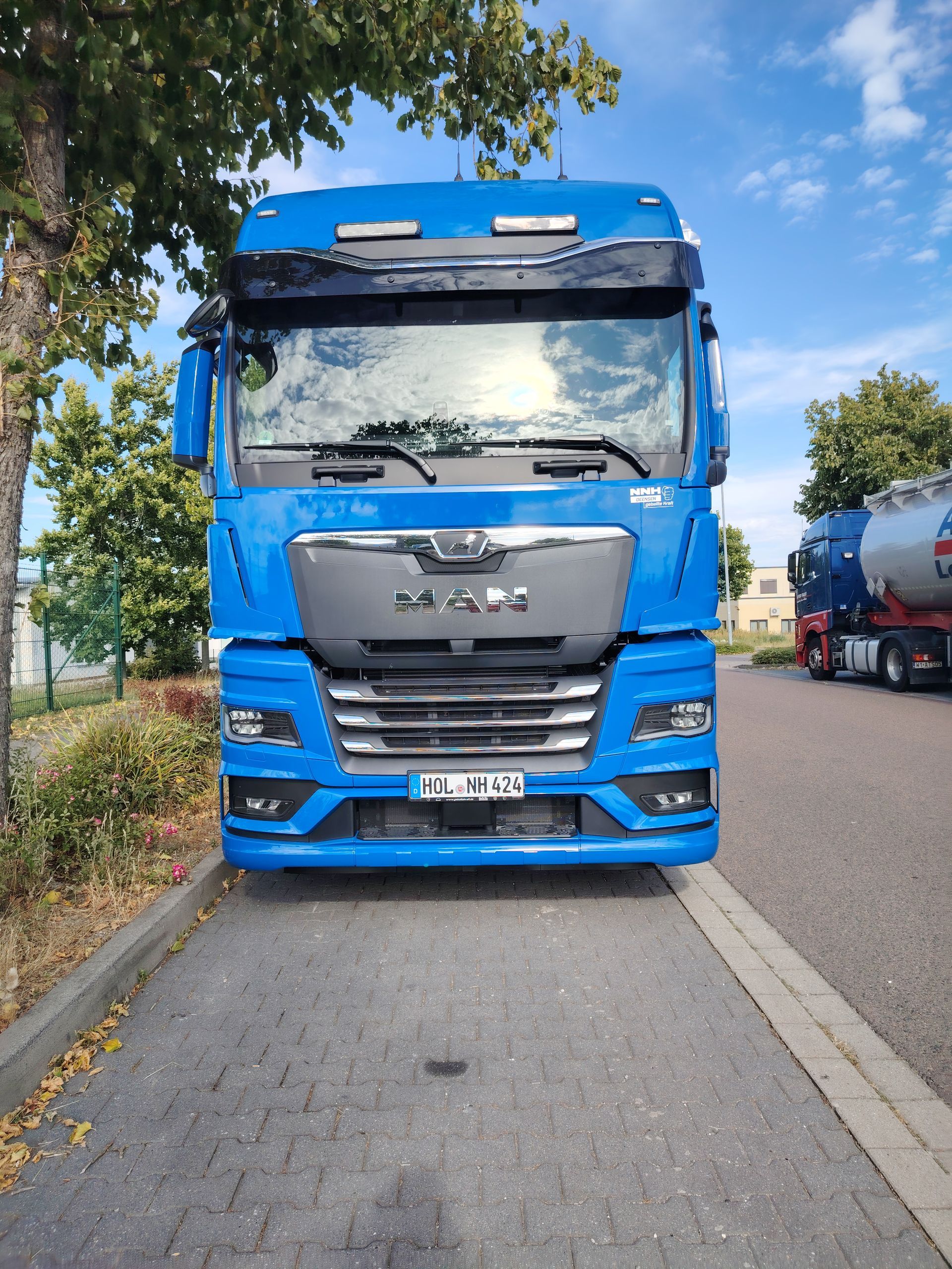 Blauer MAN-LKW auf Asphalt geparkt, Bäume an der Seite. Im Hintergrund ist ein weiterer Tankwagen zu sehen.