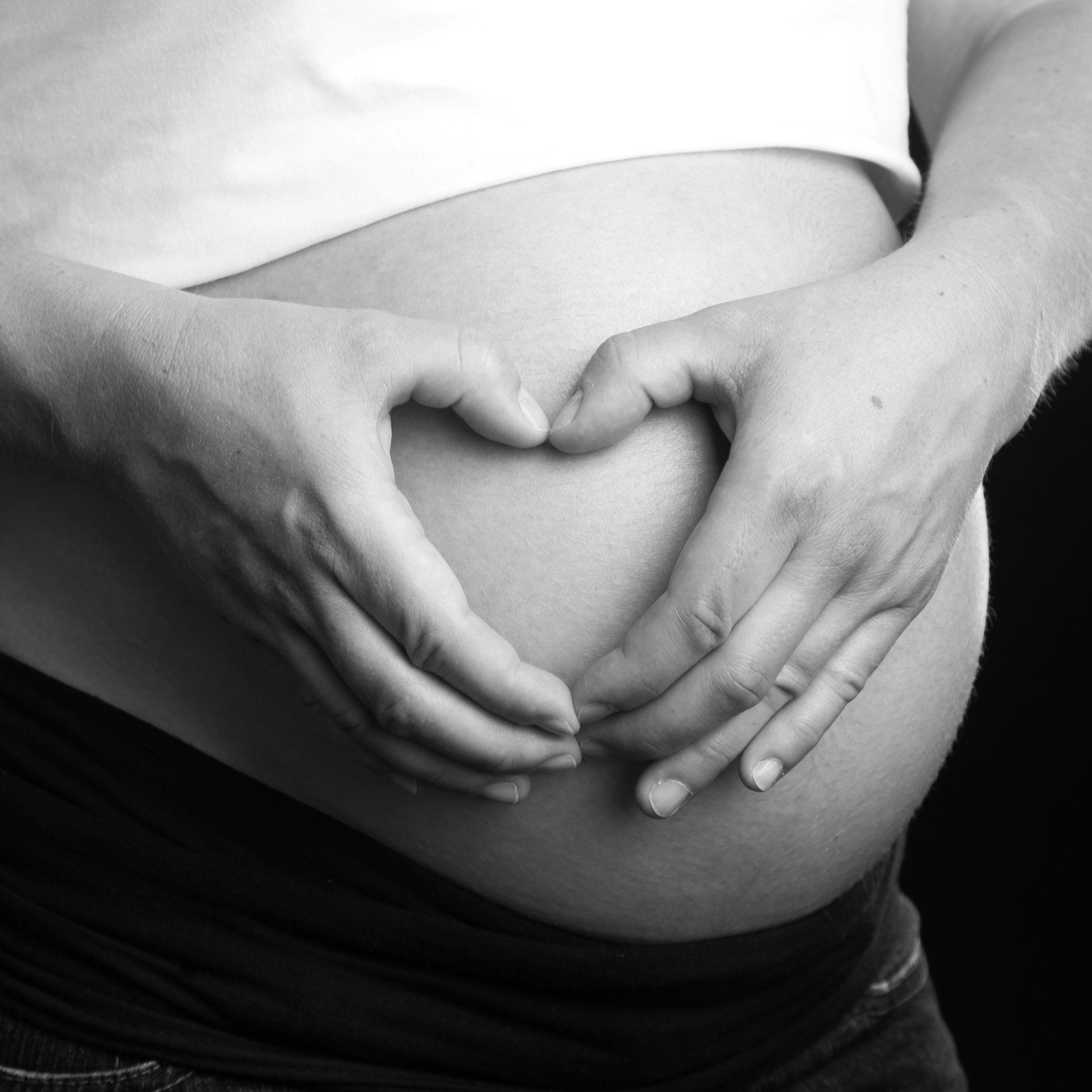 Doigts en forme de coeur sur le ventre d'une femme enceinte