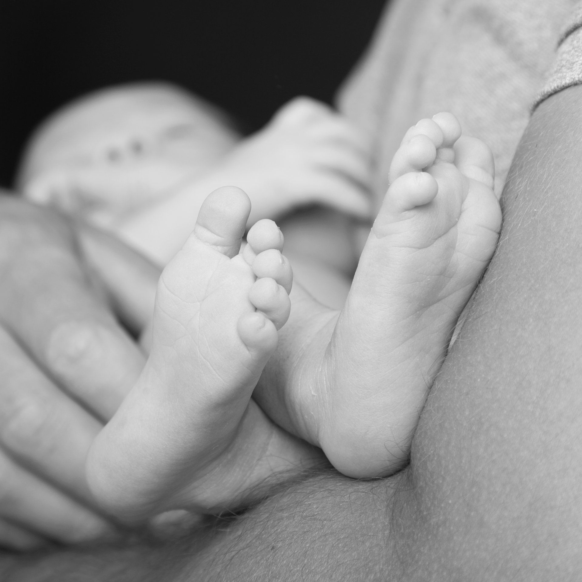 Zoom sur les pieds d'un bébé, dans les bras d'un adulte