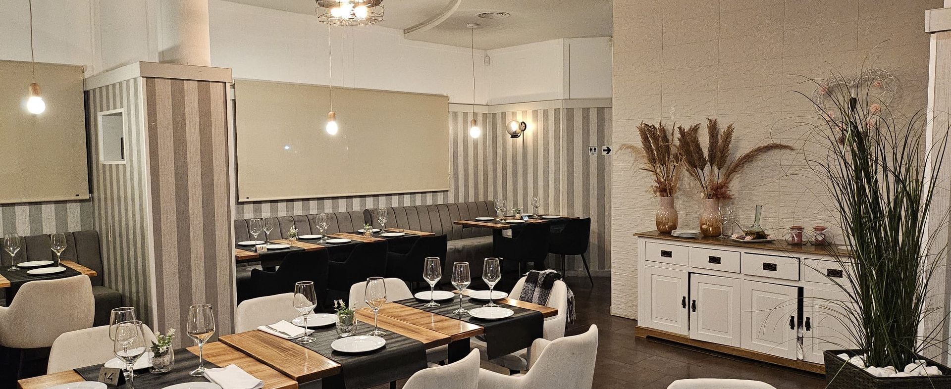 Comedor moderno con mesas puestas, decoración blanca y cortinas a rayas.