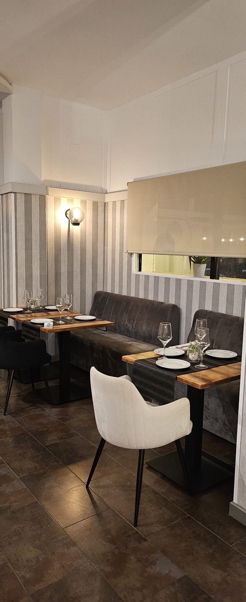 Acogedor comedor de restaurante con sillas tapizadas en tonos oscuros, mesas blancas y una iluminación tenue en las paredes.
