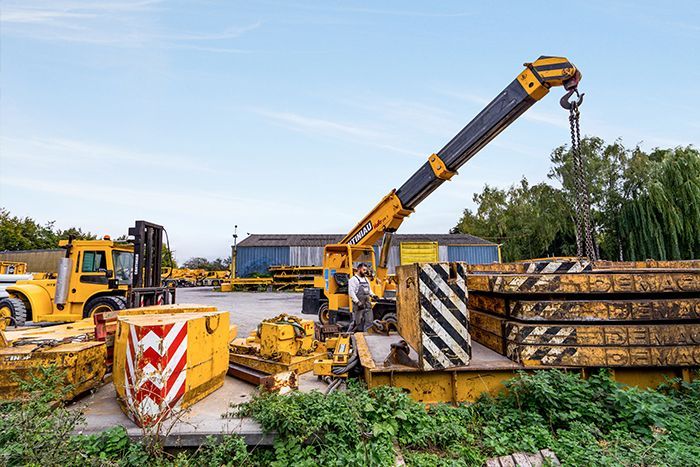 Engin de levage dans le parc de l'entreprise avec d'autres éléments autour.