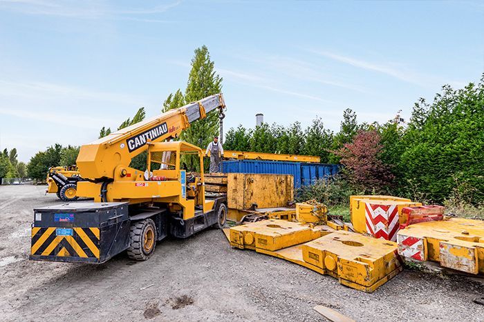 Camion-grue devant un conteneur bleu.