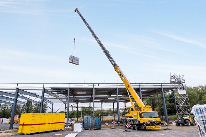 Grue de levage de Cantiniau sur chantier en train de soulever un gros bloc de pierre.