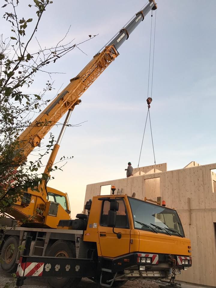 Camion grue en train de porter un élément pour constuire une maison.
