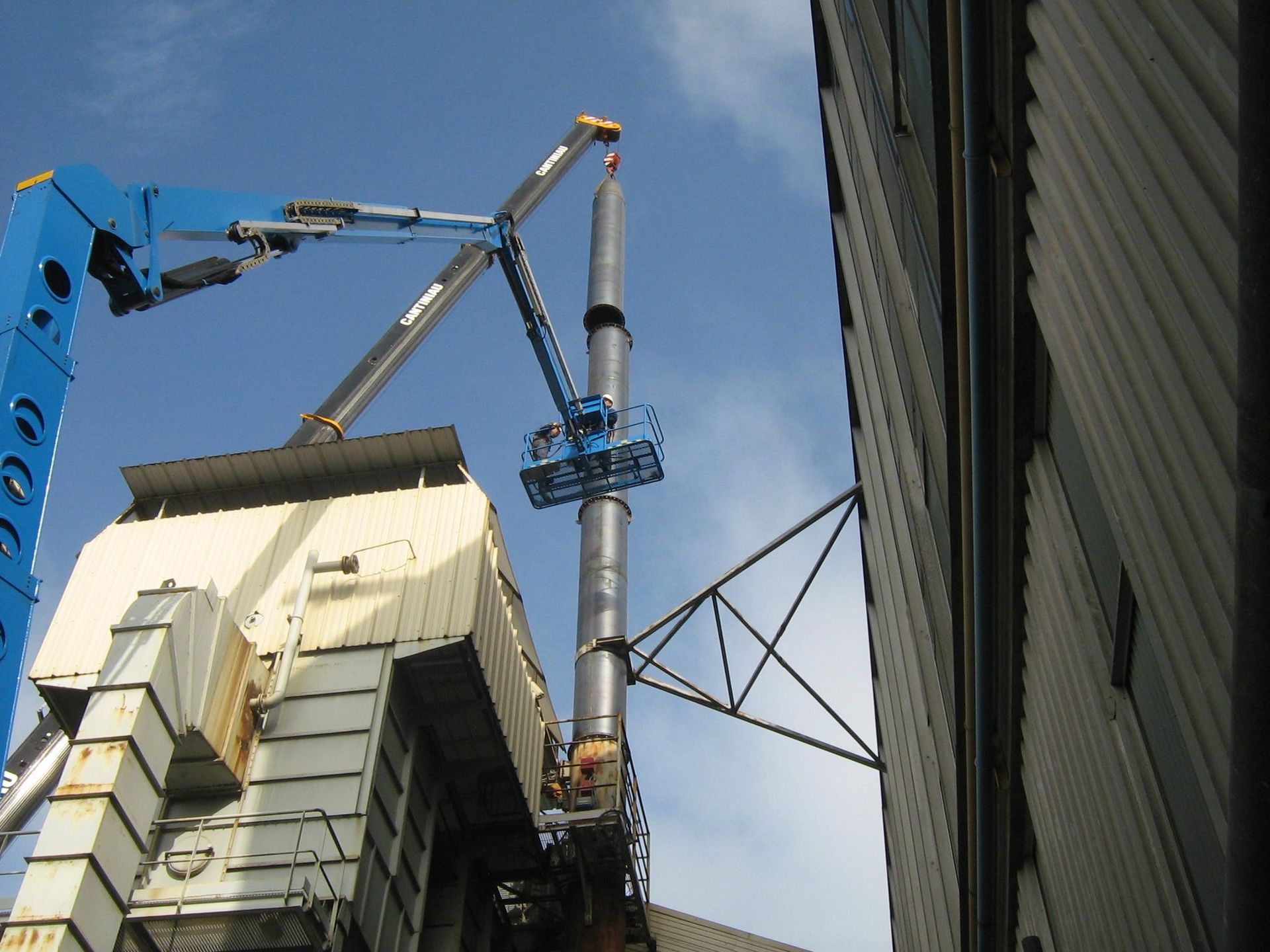Une nacelle bleue déployée prêt d'une; cheminée industrielle.