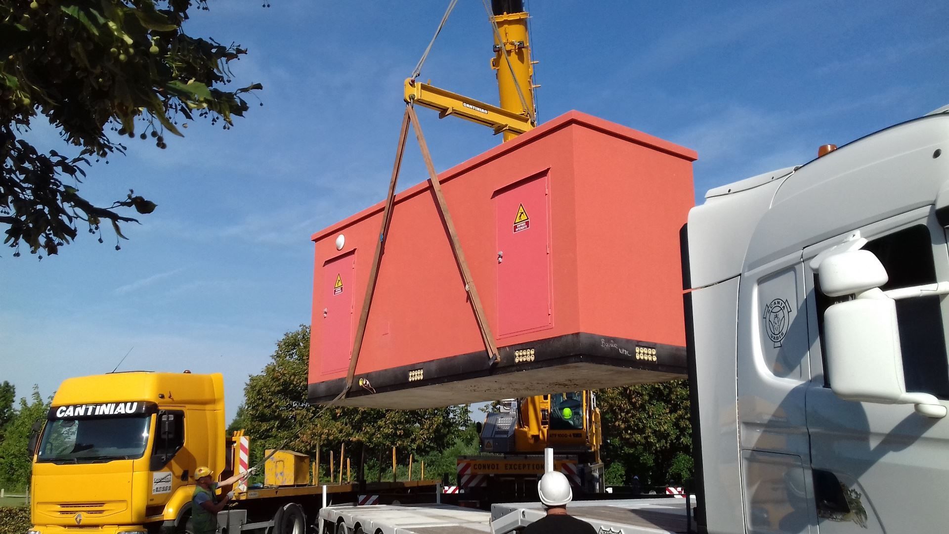 Une grue soulève une grande boîte rouge.