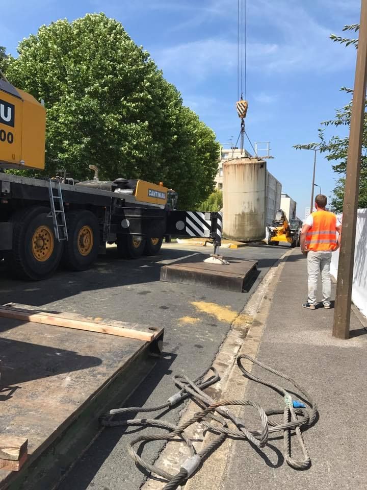 Une grue soulève un gros morceau de bois sur le trottoir.