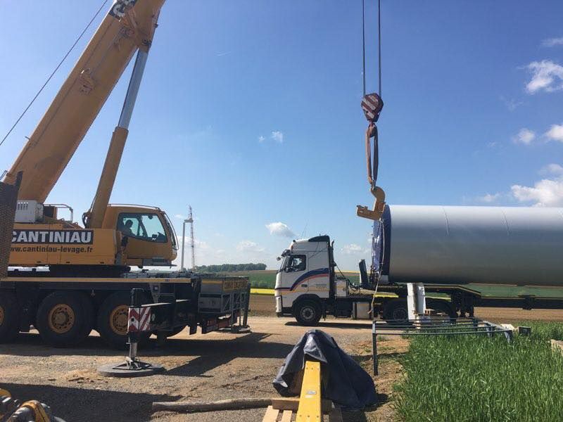 Une grue soulève un grand réservoir métallique sur un camion.