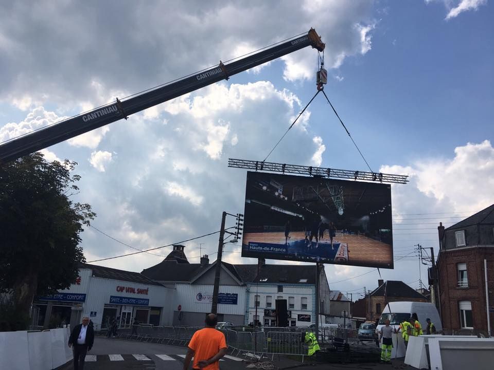 Une grue soulève un grand panneau d'affichage dans la rue.