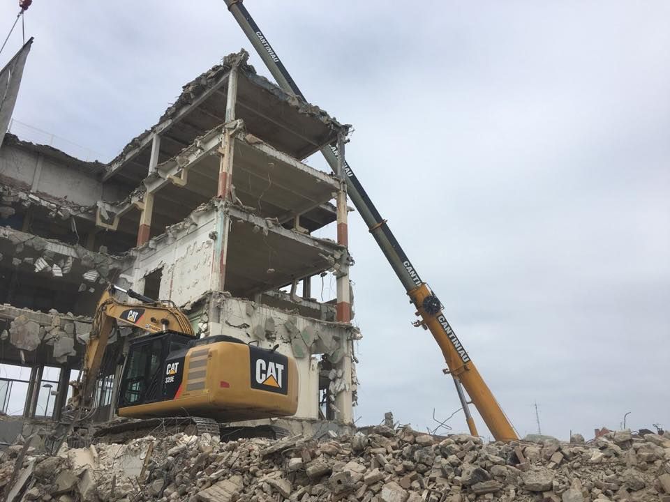 Une grande grue exor jaune soulève des décombres dans un bâtiment.