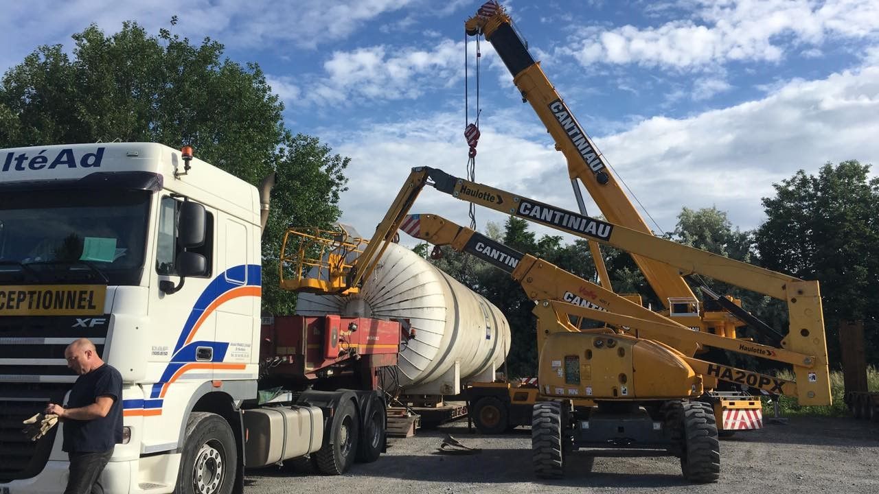 Une grue soulève un gros tuyau dans le camion.
