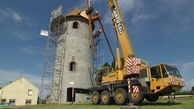 Une grue soulève une grande tour dans le sol.