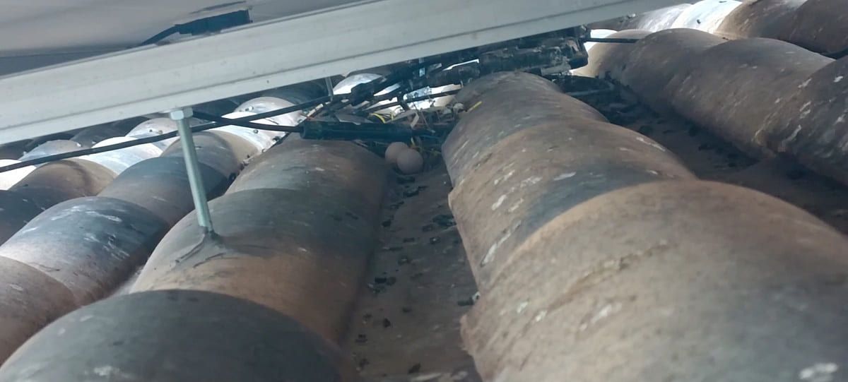 Filas de grandes tanques o tuberías cilíndricas oscuras en un espacio industrial estrecho.