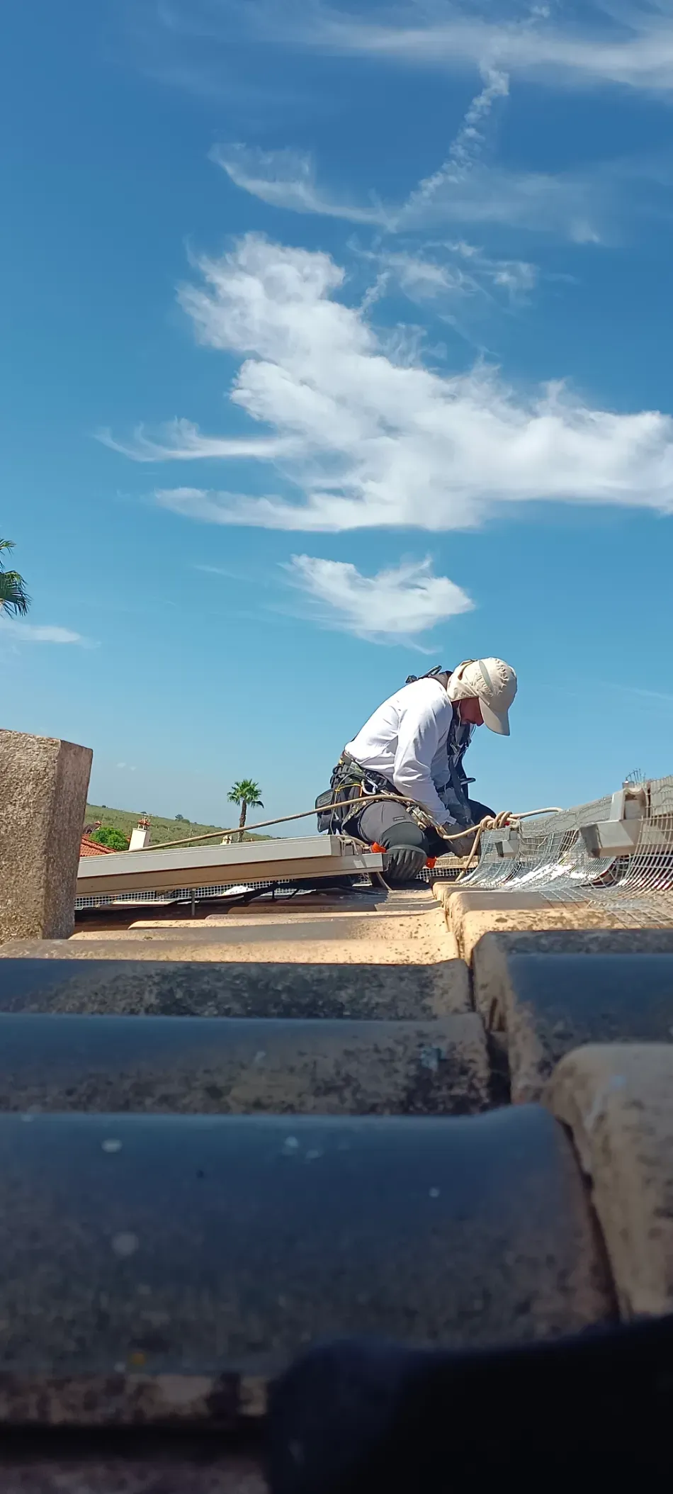 Obrero de la construcción arrodillado en una azotea bajo un cielo azul, trabajando cerca de ladrillos y bloques de hormigón.